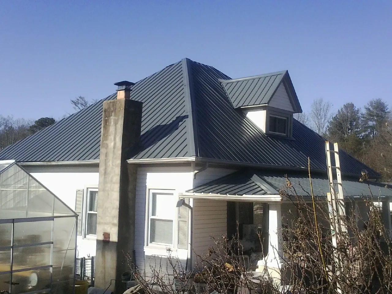 Dark blue standing seam metal roof on a white farmhouse with dormer — Slate & Tile Roof Repair by Roofing Brothers in Adair