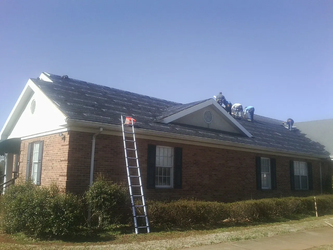 Crew tearing shingles off a brick ranch roof with a ladder set — Emergency Roof Repair work by our crew in Adair