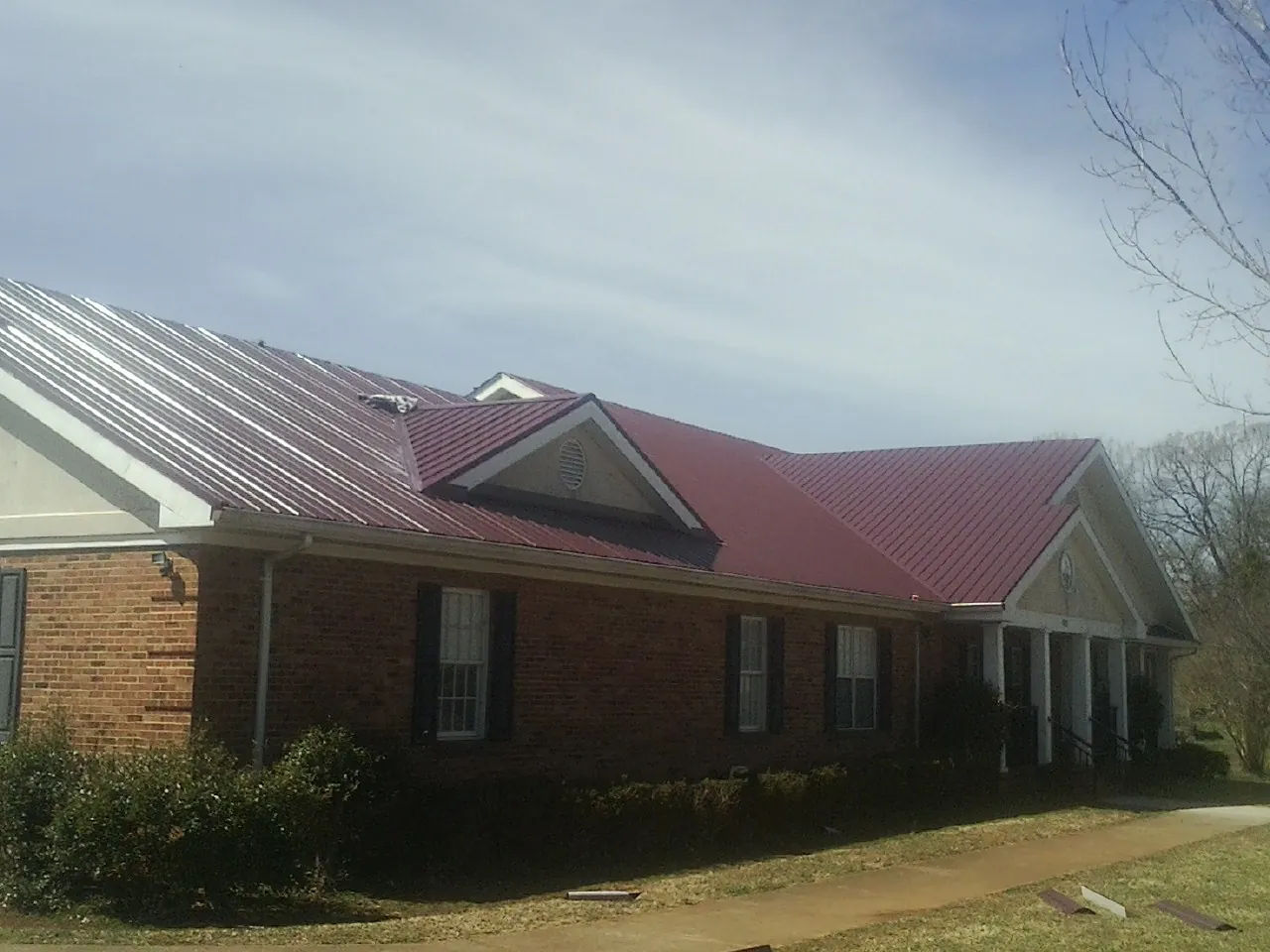 Red metal roof with gabled entries on a long brick building, from a Hail Damage Roof Repair job in Adair