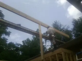Carpenter setting a ridge beam over a new addition frame in Adair