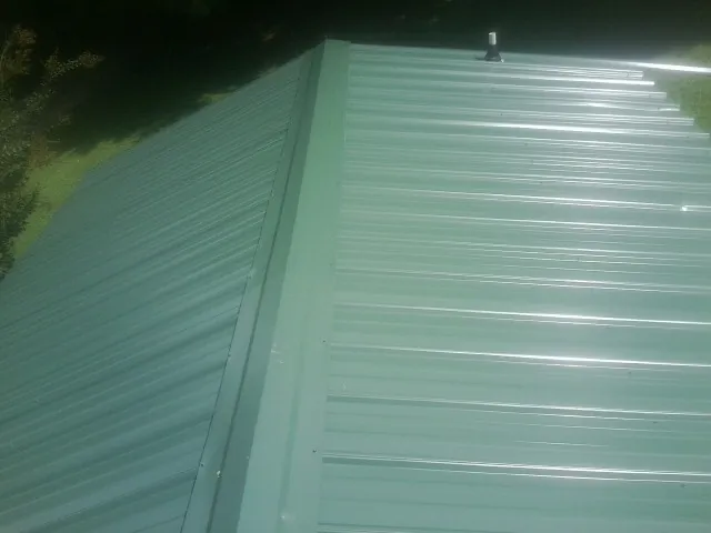 New green metal panels meeting at the ridge of a roof — Flat Roof Repair work by our crew in Adair