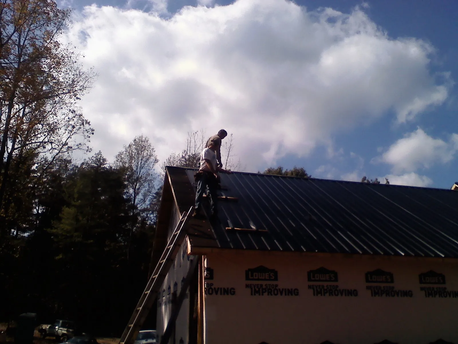 Roofer fastening dark metal panels high against a cloudy sky, from a Roof Inspection job in Adair